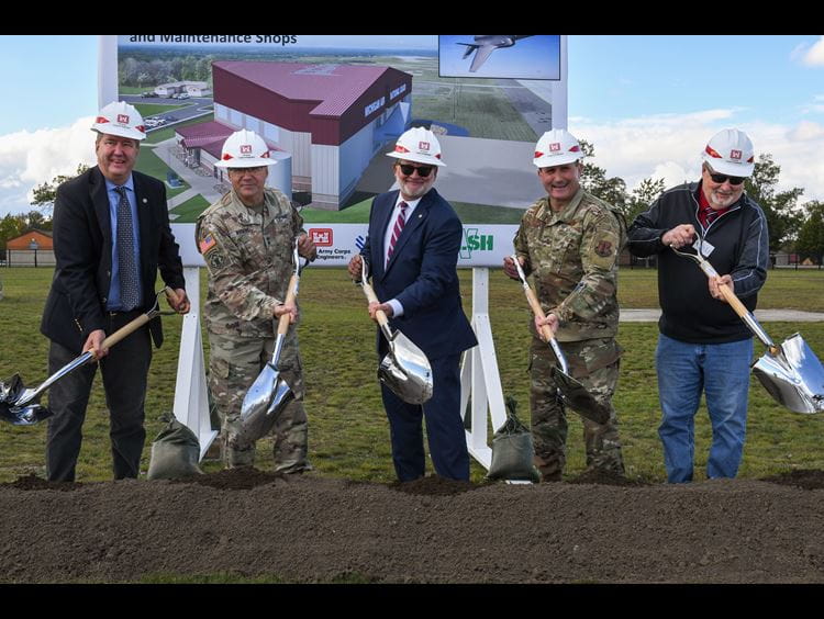 light-skinned men wearing hardhats shoveling dirt at ceremony