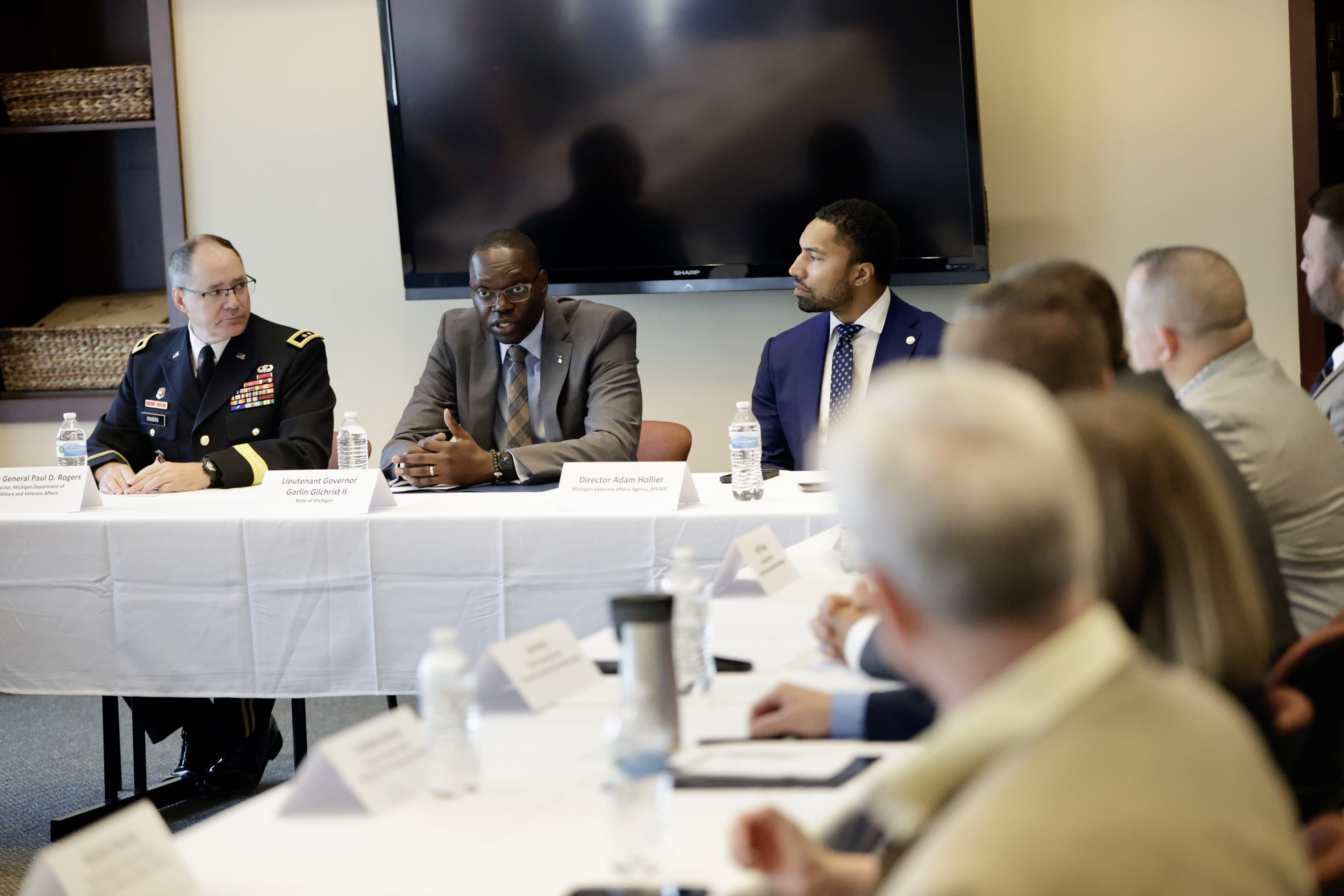 Light and dark-skinned men sit at a white draped table during a discussion