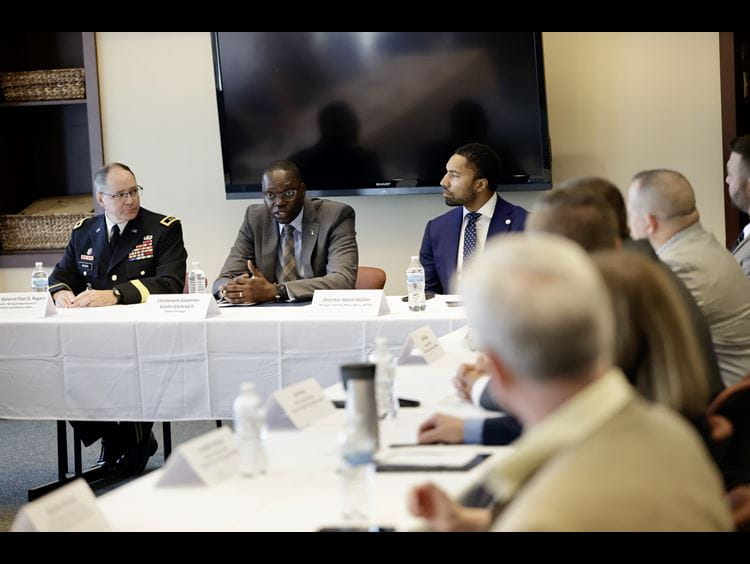 Light and dark-skinned men sit at a white draped table during a discussion