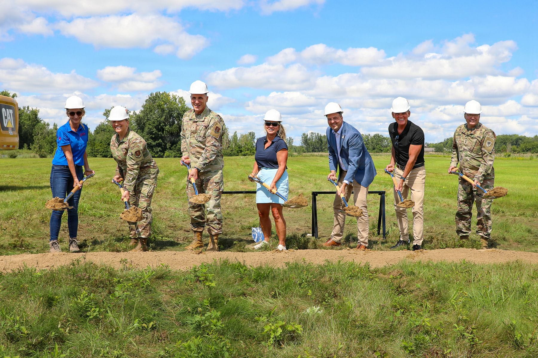 Civilian and military personnel hold shovels