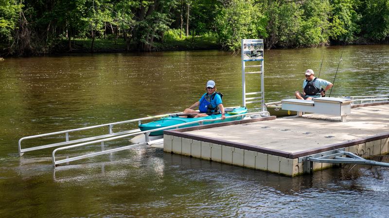 A couple of kayakers launch their boat at an accessible kayak launch