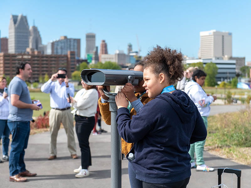 A youth visitor using a blind color viewer to look over the Detroit River
