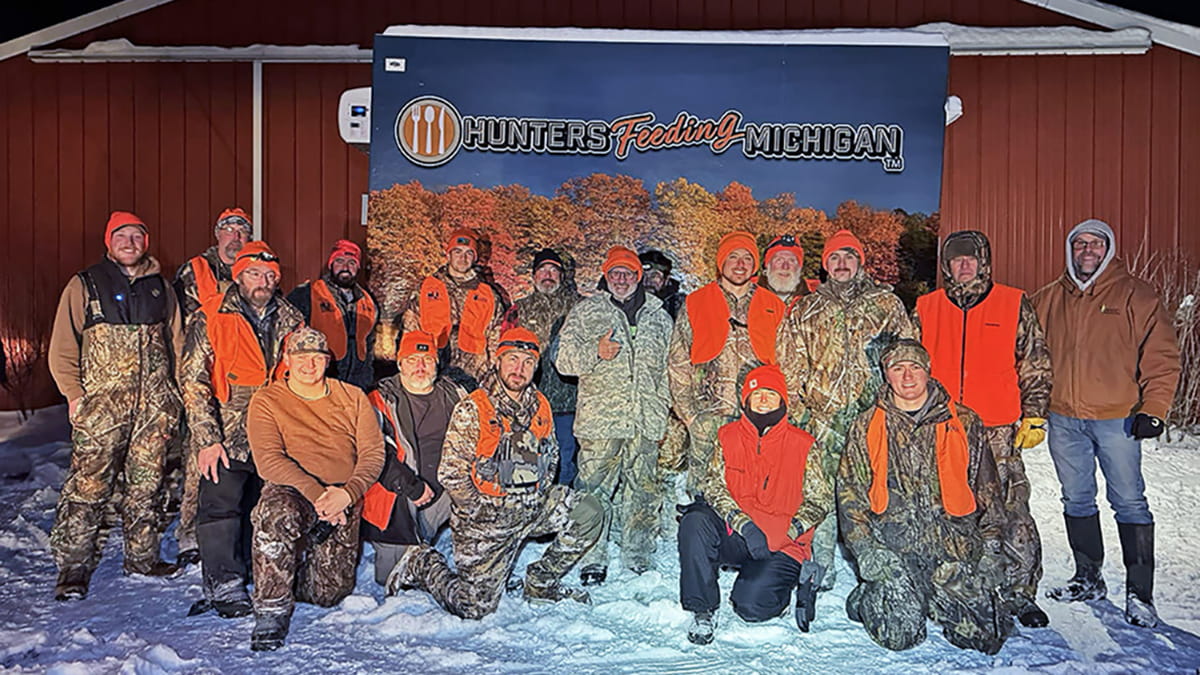 group of hunters in orange in front of Hunters Feeding Michigan banner