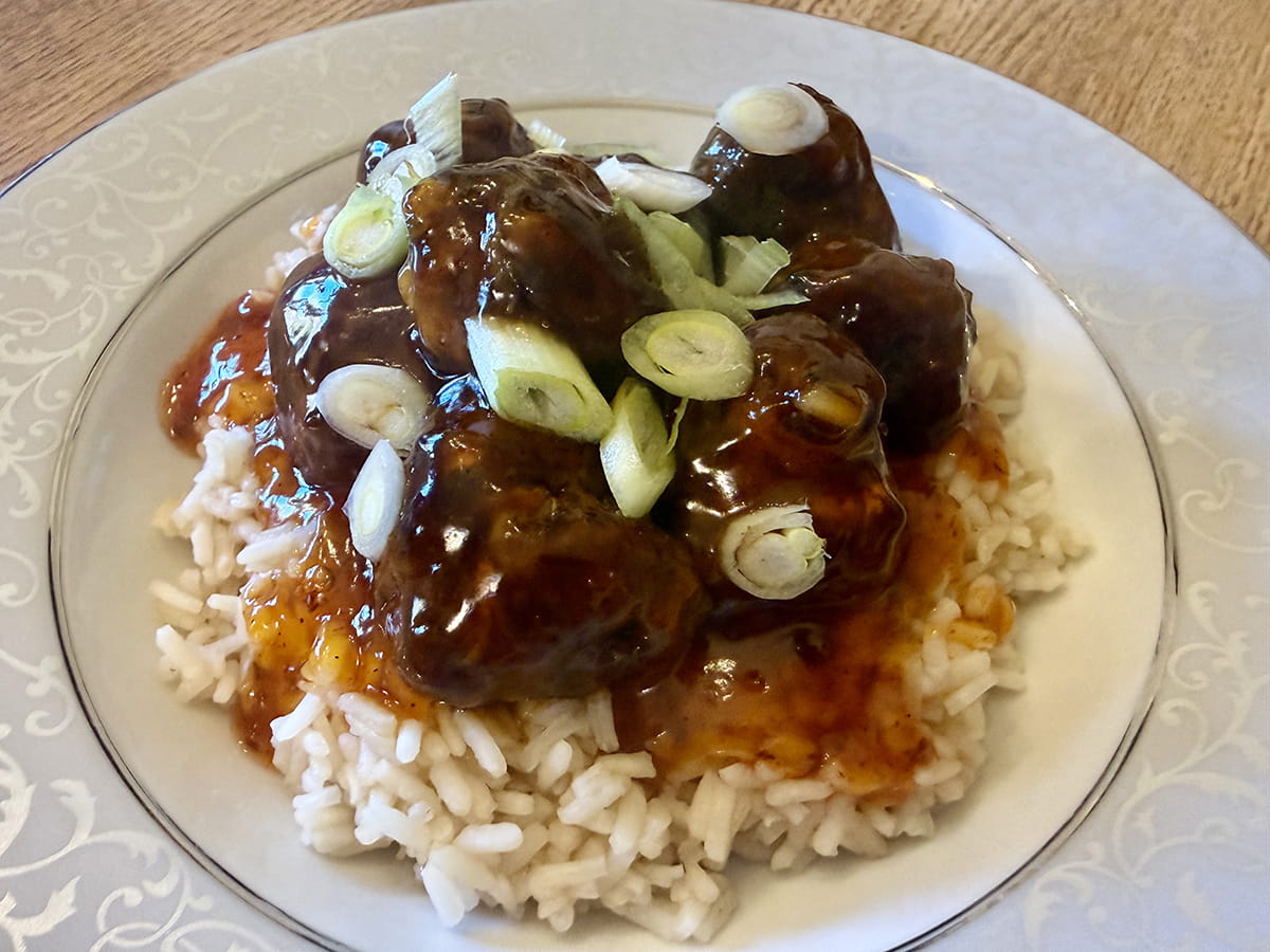 Sweet and sour venison meatballs over rice on plate