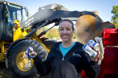 a woman holding up recyclable materials in front of a construction vehicle