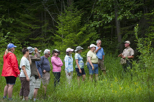 A group of educators stand in a field listening to a presentation at ANR