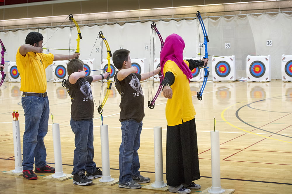 Four students line up to shoot bow and arrow at targets