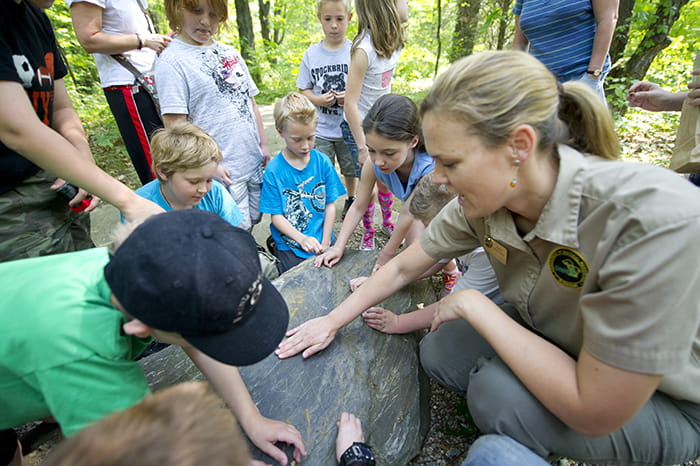 Kids touch a rock while DNR interpreter teaches them about geology