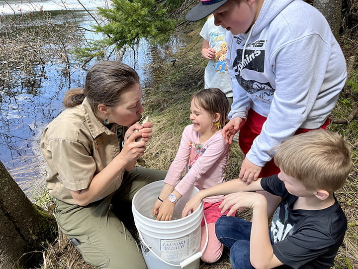 A park interpreter pretends to kiss a small fish in front of a group of children.