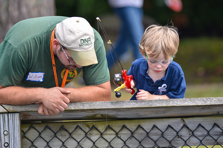 A man with a DNR cap instructs a young boy in fishing at the Pocket Park