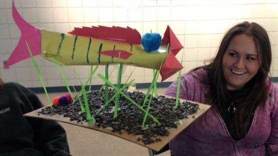 A teacher looks at a project of a paper fish and smiles