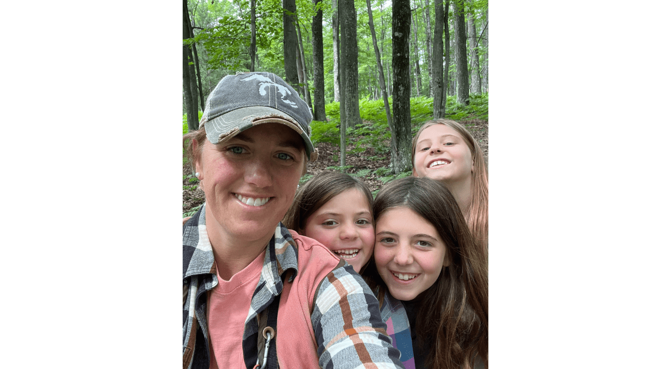 A woman and three girls pose for a picture while walking through the forest