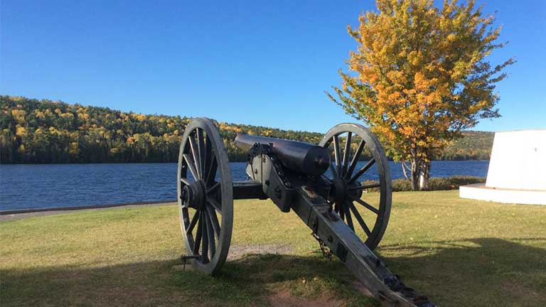 An old cannon at Fort Wilkins with fall colors on trees in background