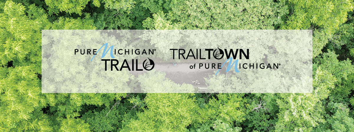 paved trail going through forested canopy, Pure Michigan Trails and Trail Town logos