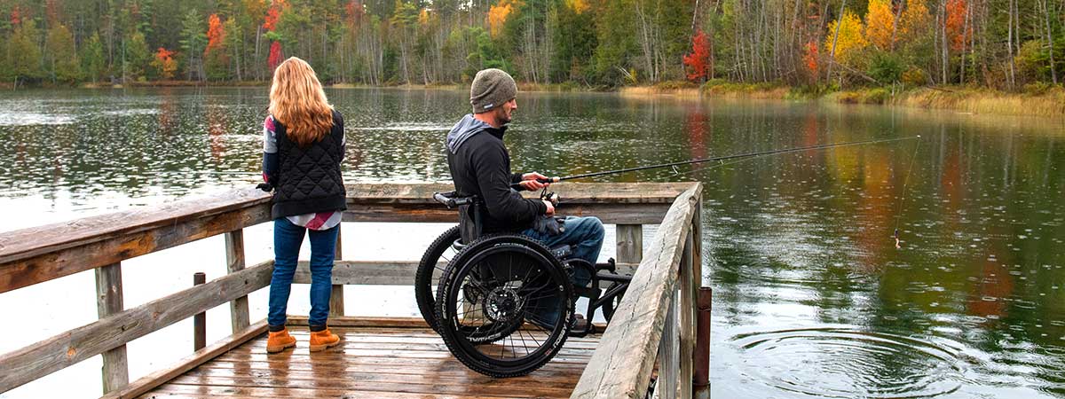 Two people fishing on a pier with fall colors in the background.