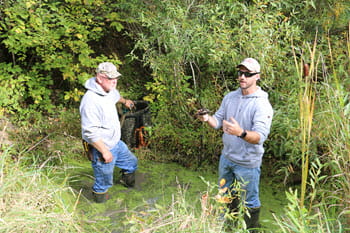 Two men stand in a puddle giving a trapping demonstration