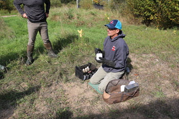 A man kneels on the ground holding a cup of bait