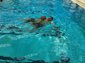 a man pulls another man through deep water in a pool