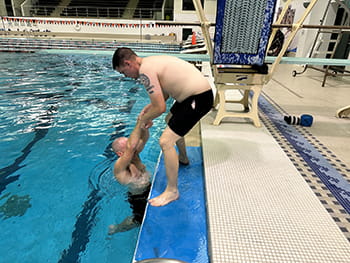 man on pool deck pulls someone out of pool