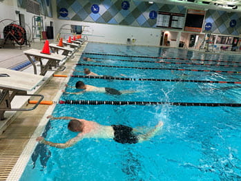 four men in a pool practice kicking and breathing