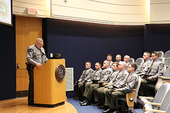 Person stands at a podium speaking to others sitting in an auditorium