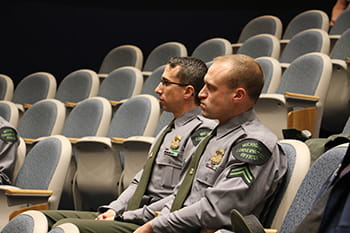 Two men sit in auditorium seats listening to a speaker