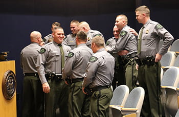 Group of men stand in auditorium, hugging each other and shaking hands