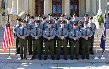 group of officers stand outside, smiling on steps with flags