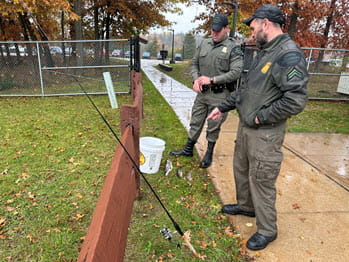 Two men talking next to a fishing pole and bucket