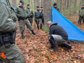 man kneeling on ground demonstrates how to make a shelter in the woods with a tarp