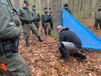 man kneeling on ground demonstrates how to make a shelter in the woods with a tarp