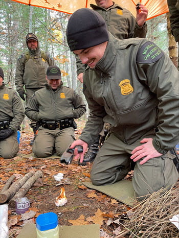 smiling man kneels on ground making a fire