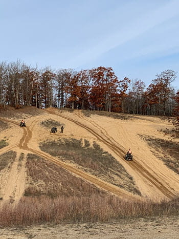 people ride off-road vehicles on a steep, sandy hill in the woods