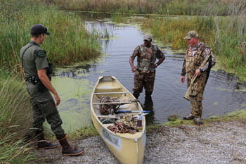 conservation officer talks to two duck hunters standing by a canoe in a pond during a scenario