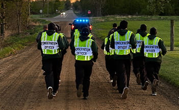 Group of people run on a dirt road behind a law enforcement vehicle