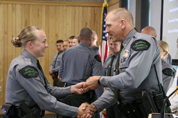 A man presents a badge to a young woman while they shake hands