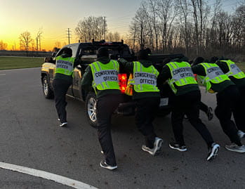 Six people pushing a truck outside on a track