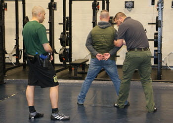 A survival tactics instructor demonstrates proper officer positioning to a student inside a gym