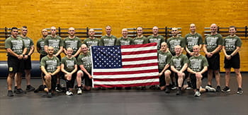 group of people standing together in a gym, smiling with an American flag