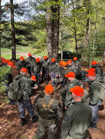 group of people gather, listen to instructor in the woods