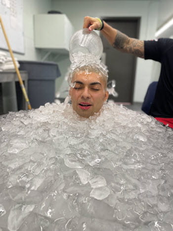 A man sitting in a tub of ice has ice poured over him
