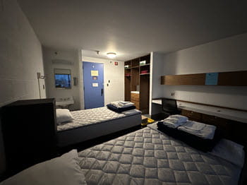 dorm style bedroom with two beds, a sink, desk and closet