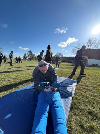 person outside on a mat performs survival tactics moves on a mannequin