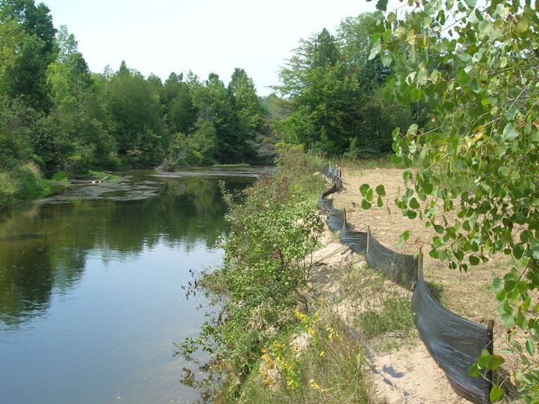 A river with a steep bank with a fence on the top of the bank