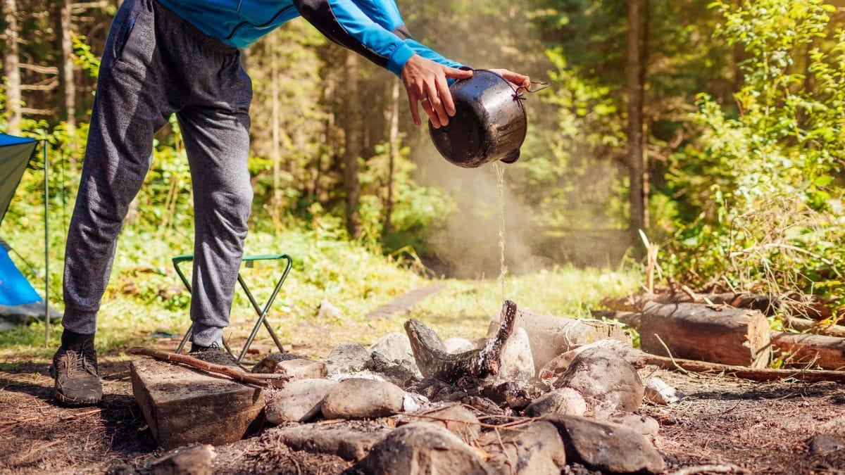 A camper pours water to put out a fire