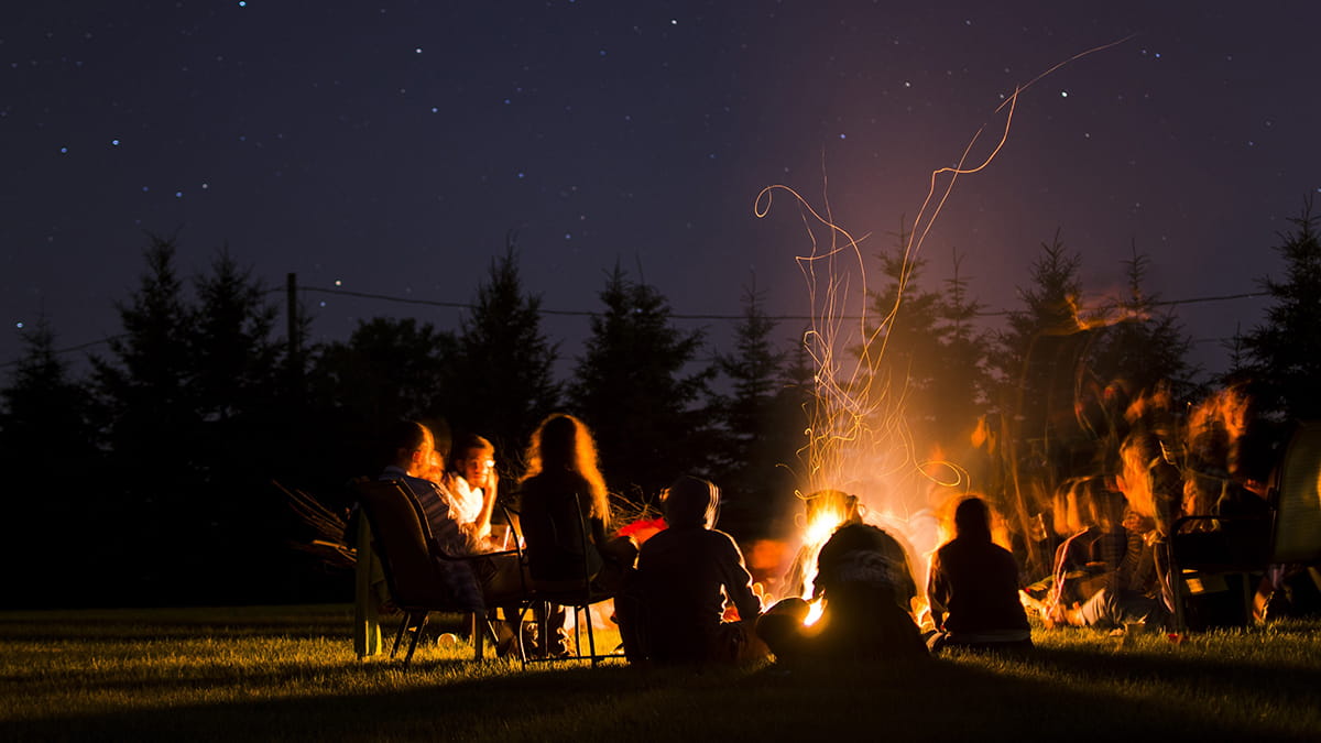 A group of people gather around a campfire under the stars