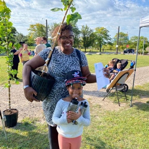 A guardian and child hold a sapling that they are excited to plant