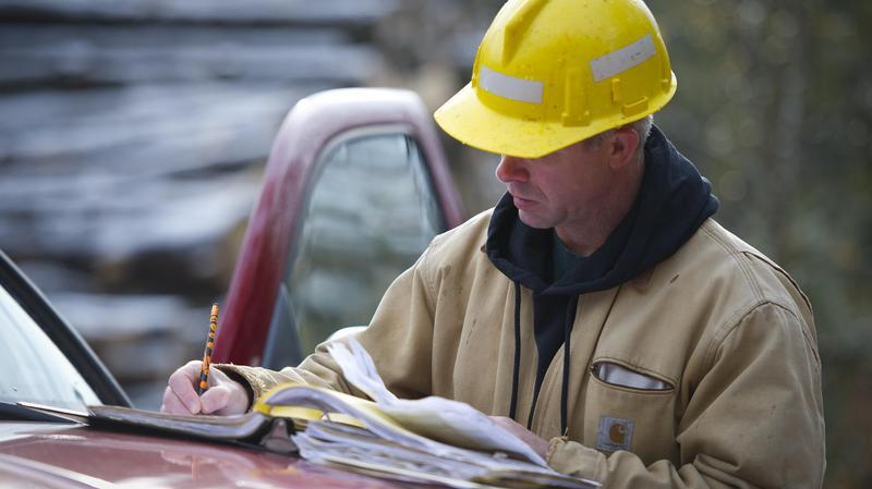 A forester fills out paperwork on the hood of a red truck during a timber sale