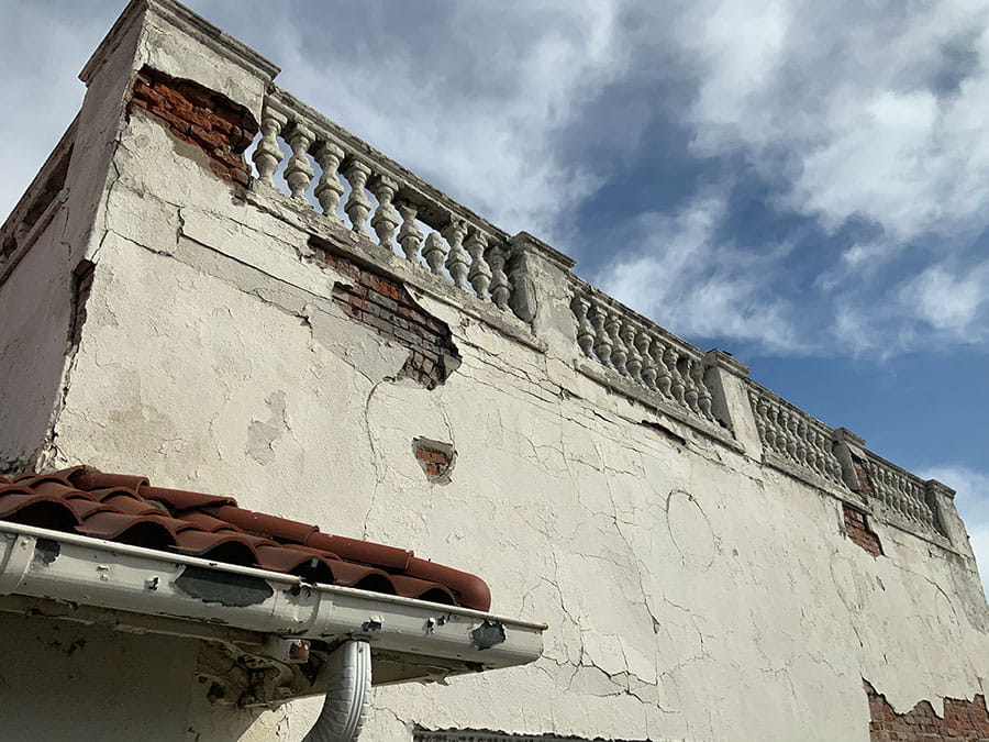 Exterior top of side of building with spalling stucco and brick exposed in some parts.