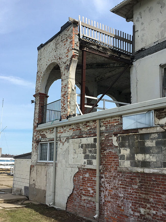 Exterior balcony with deteriorated brick siding exposed under concrete.